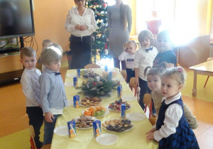 Pani dyrektor Maria Królikowska, pani Anna Tylman oraz dzieci stoją wokół stołu z poczęstunkiem.